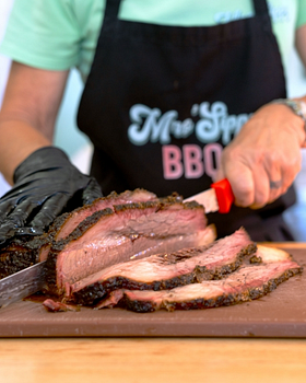 Pitmaster slicing freshly smoked brisket in a Mrs'Sippy BBQ apron